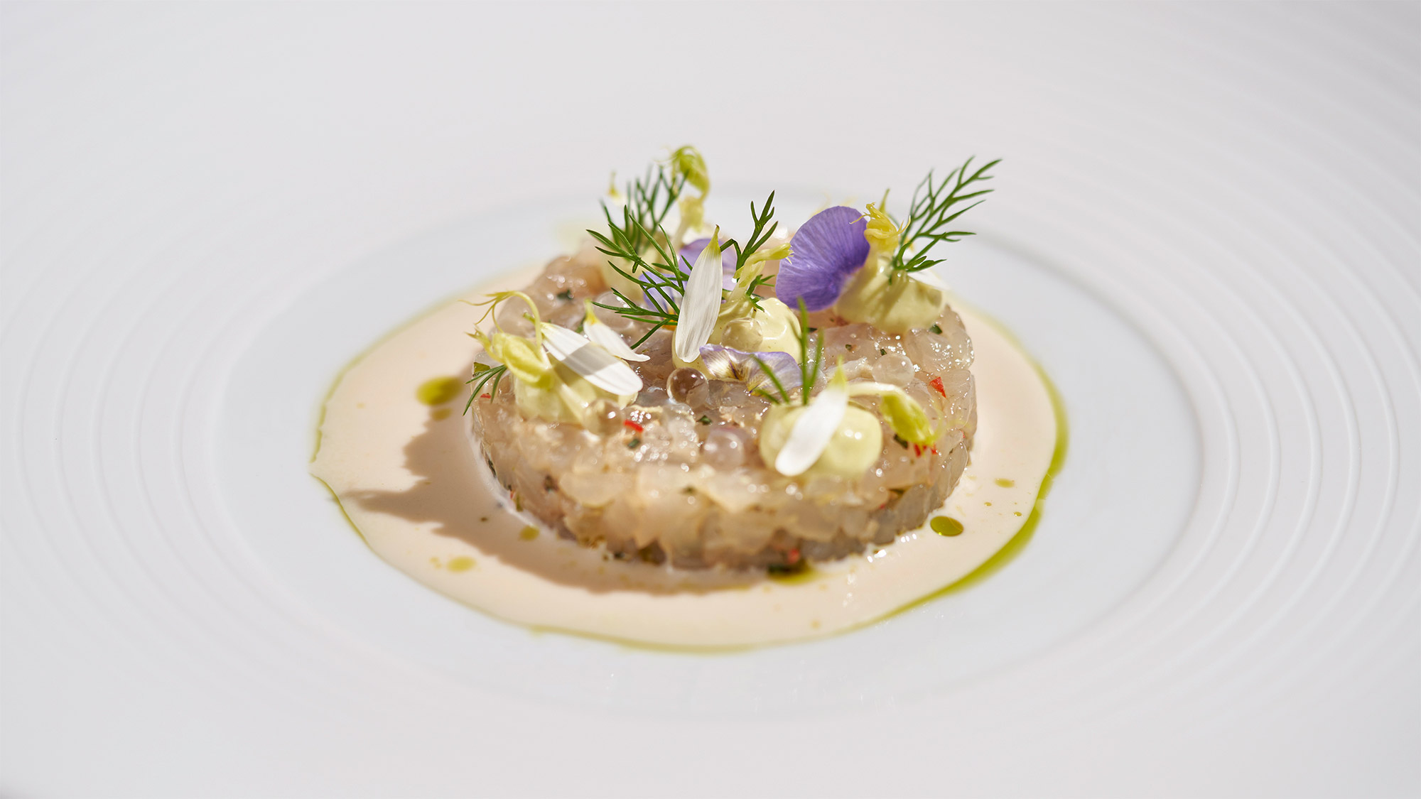 Tartare de poisson avec fleurs et herbes sur une assiette blanche.