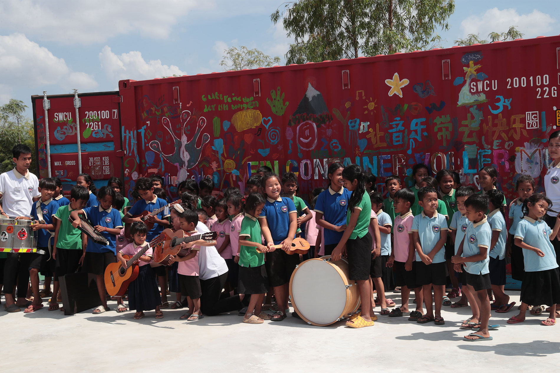 Des enfants et des adultes avec des instruments devant un conteneur peint de couleurs vives.