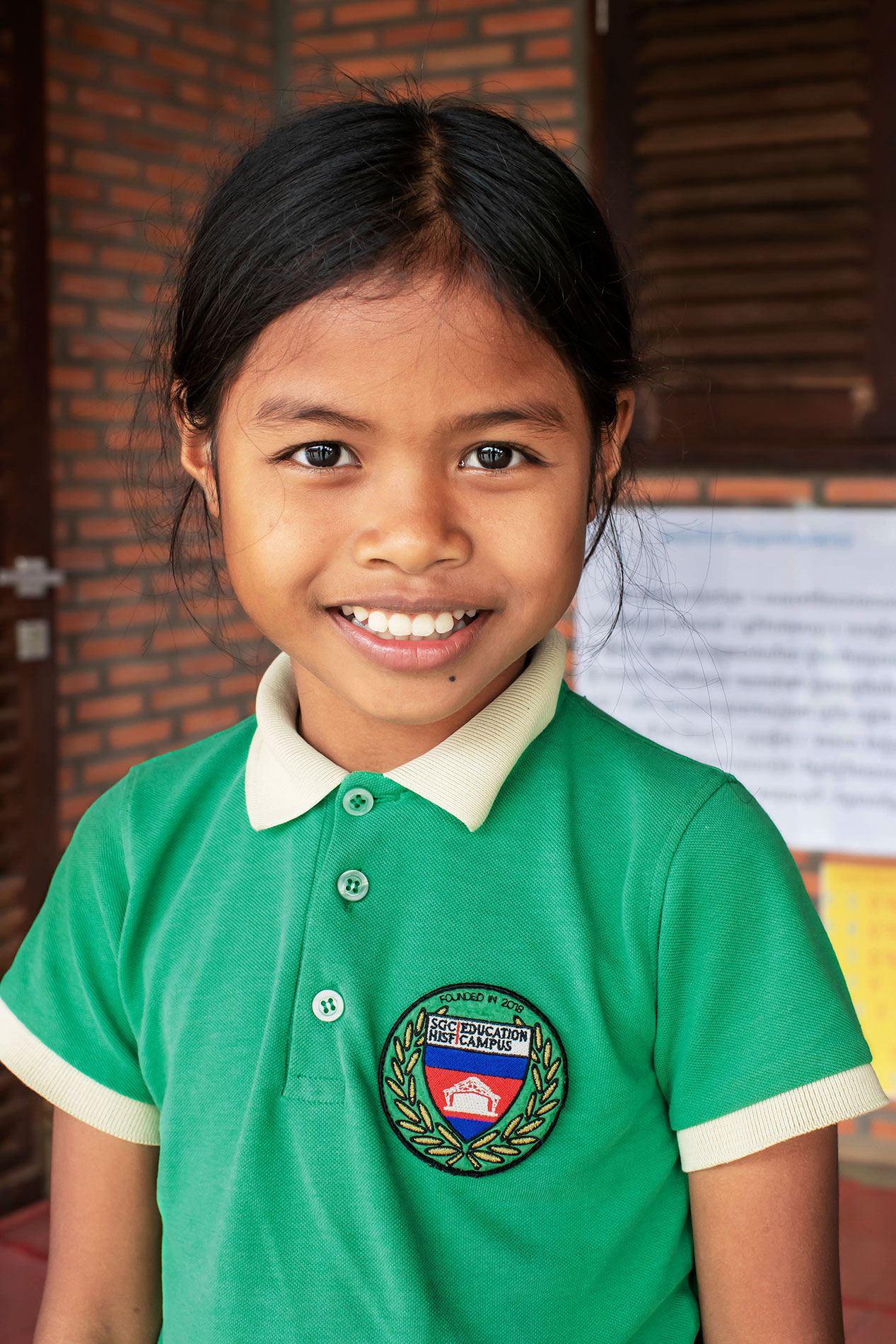 Une élève souriante en polo scolaire vert.