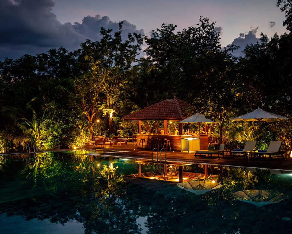 Beleuchtete Poolbar mit Spiegelungen im Wasser am Abend.